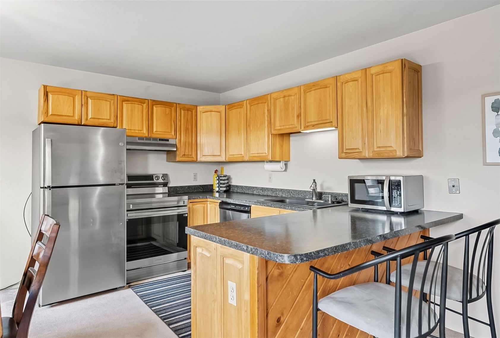 9849 Ryan Gulch Road, Unit 203 Silverthorne, CO 80498 - Photo 14 of 35 Kitchen with appliances with stainless steel finishes, dark countertops, a peninsula, a breakfast bar, and under cabinet range hood