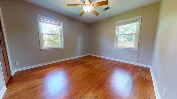a view of an empty room with wooden floor and a window