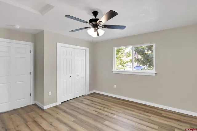 a view of an empty room with wooden floor and a ceiling fan