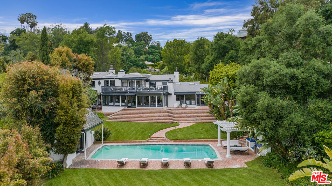 a view of pool with lawn chairs and large trees