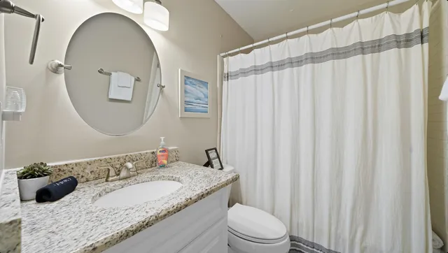 a bathroom with a granite countertop sink vanity mirror bathtub shower and a toilet