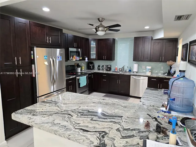 a kitchen with stainless steel appliances kitchen island granite countertop a sink refrigerator and cabinets