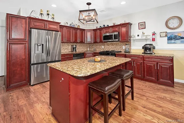 a kitchen with stainless steel appliances granite countertop a refrigerator a stove a sink dishwasher and wooden cabinets with wooden floor