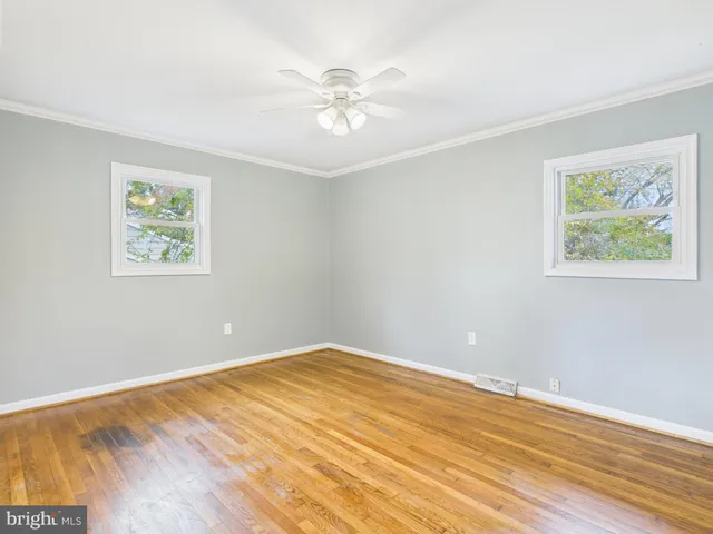 a view of an empty room with wooden floor and a ceiling fan