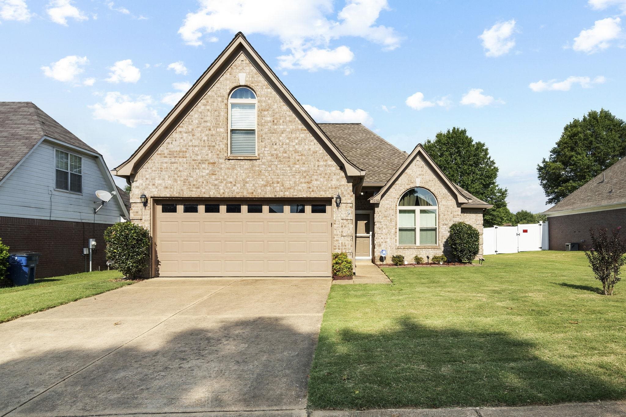 View of front facade with brick siding, a garage, driveway, and a gate