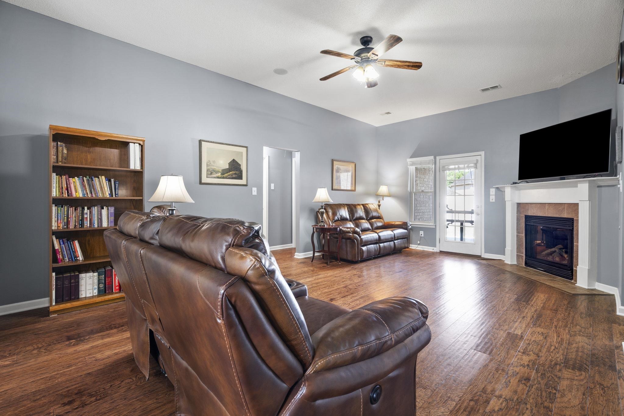 Living room with dark wood-type flooring, a tile fireplace, and a ceiling fan