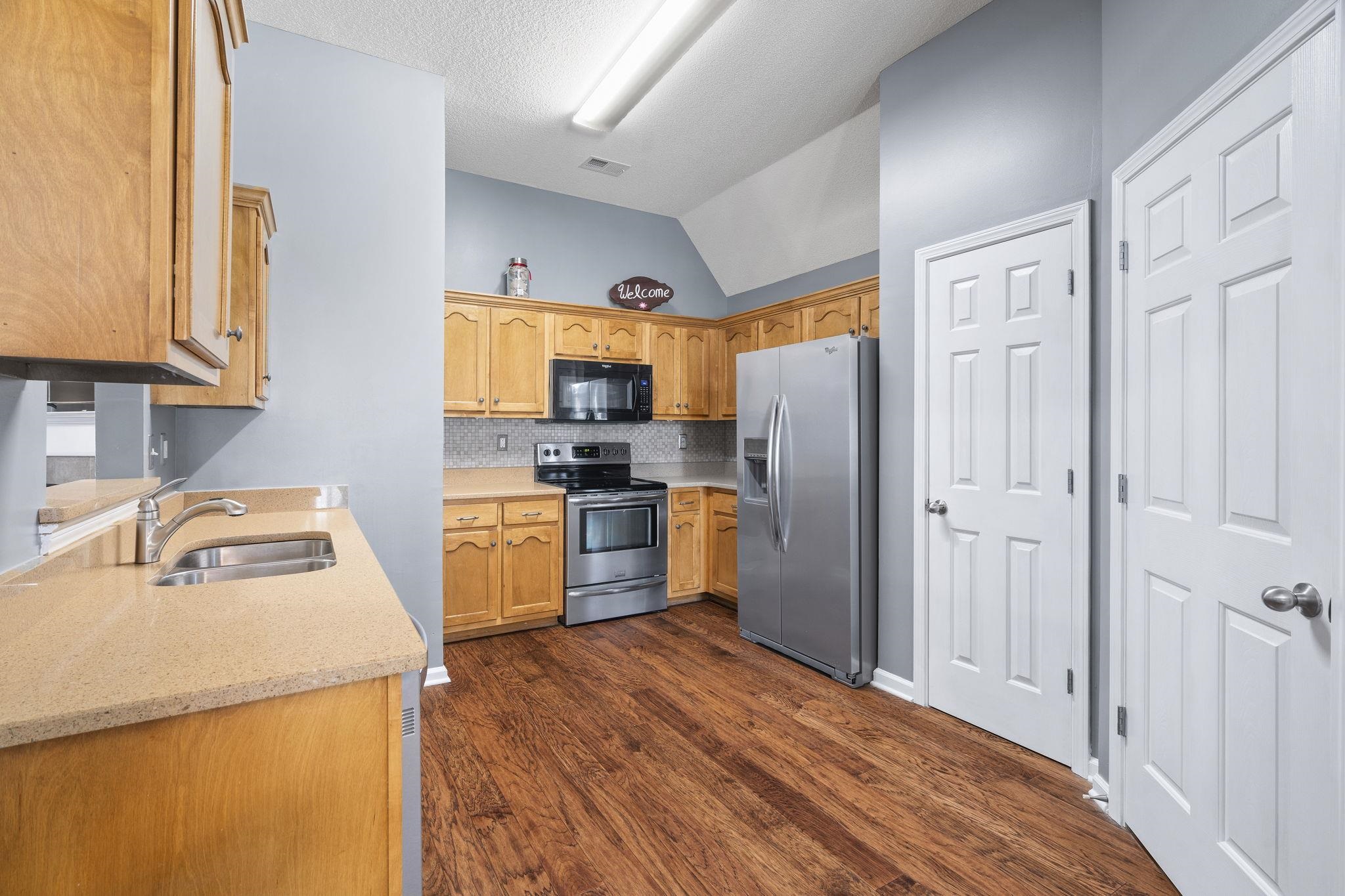 Kitchen with lofted ceiling, appliances with stainless steel finishes, dark wood-style floors, tasteful backsplash, and light stone counters
