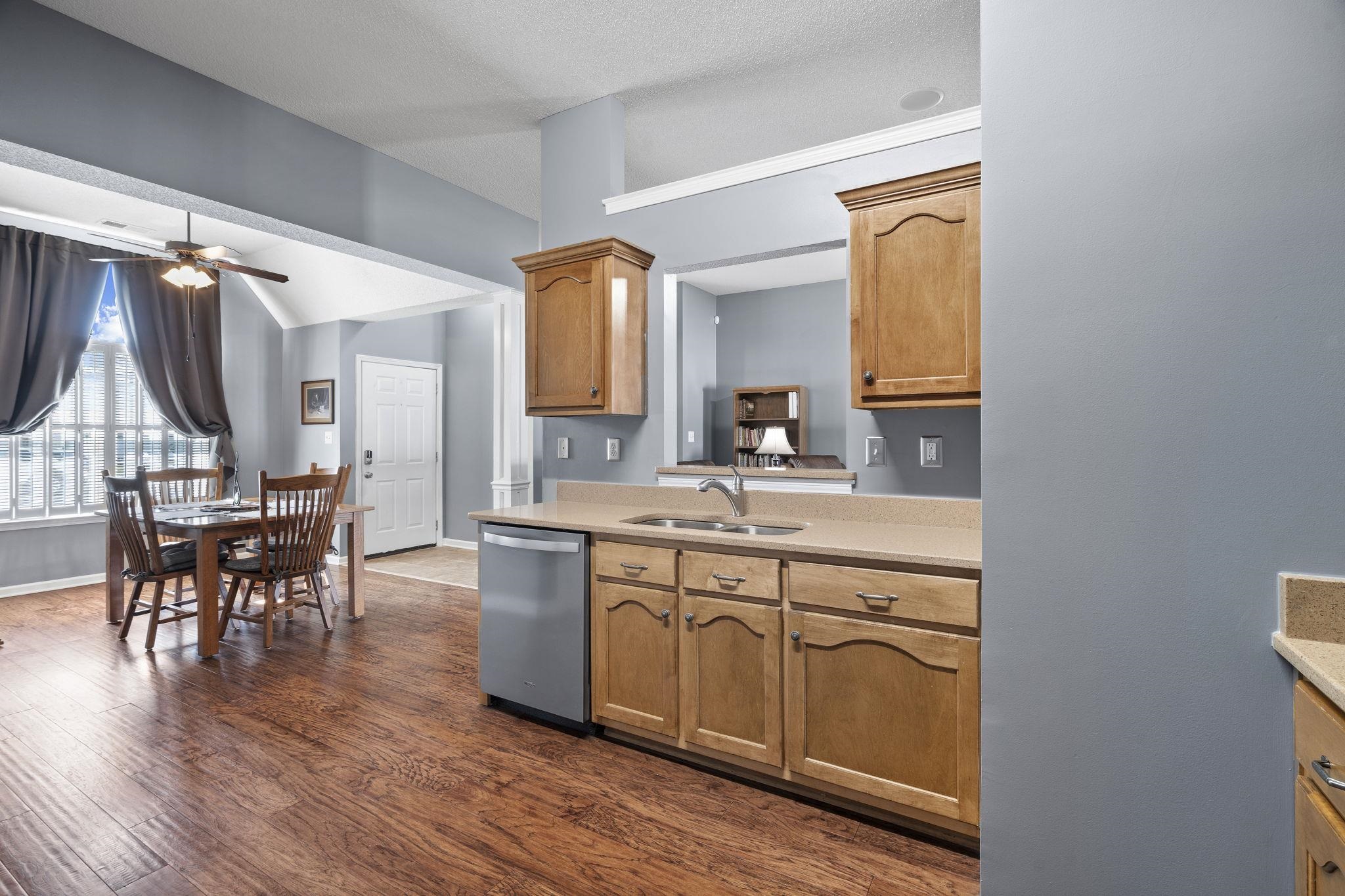Kitchen with dark wood-type flooring, ceiling fan, stainless steel dishwasher, lofted ceiling, and light stone counters