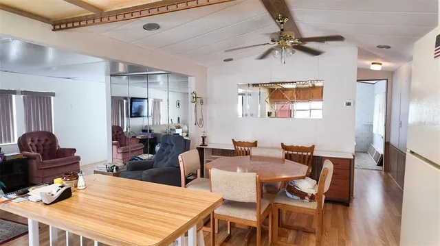 a dining room with wooden floor a chandelier fan a wooden table and chairs