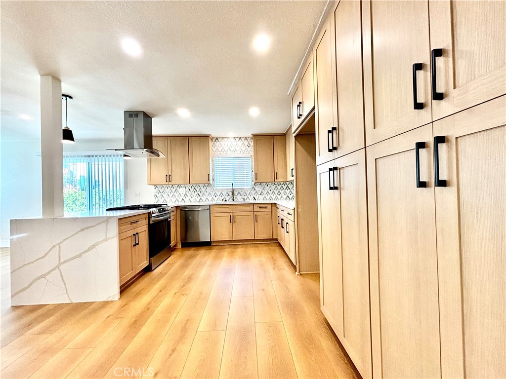 6210 Halstead Avenue, Unit A Rancho Cucamonga, CA 91701 - Photo 23 of 32 a large white kitchen with stainless steel appliances kitchen island granite countertop a refrigerator a sink dishwasher a stove and white cabinets with wooden floor