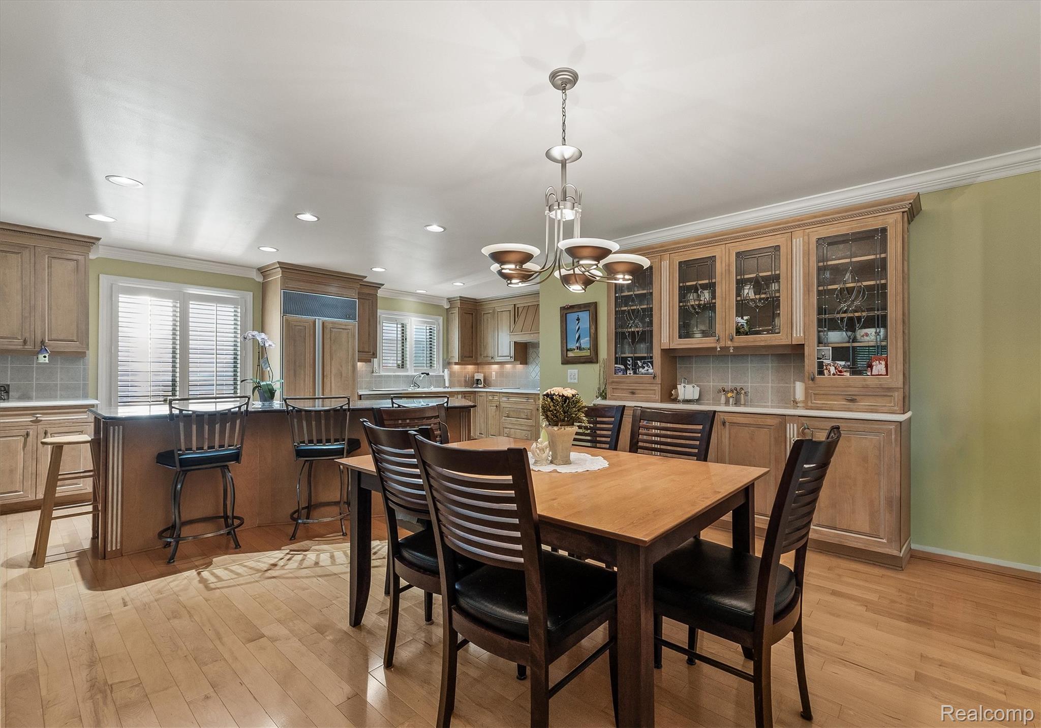 1662 Sumac Drive Rochester, MI 48309 - Photo 10 of 38 Open-concept kitchen and dining area featuring light wood-finish flooring, custom wood cabinetry, a central island with countertop seating, recessed lighting, and a chandelier over the dining table