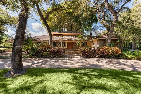 a view of house in front of a big yard with large trees