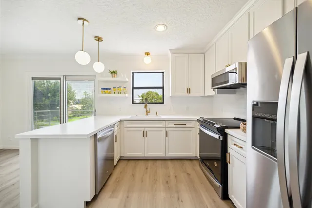 a kitchen with stainless steel appliances granite countertop a sink a stove a refrigerator with white cabinets and wooden floor