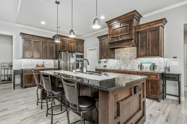 a kitchen with stainless steel appliances granite countertop a stove a sink dishwasher a refrigerator and a dining table with wooden floor