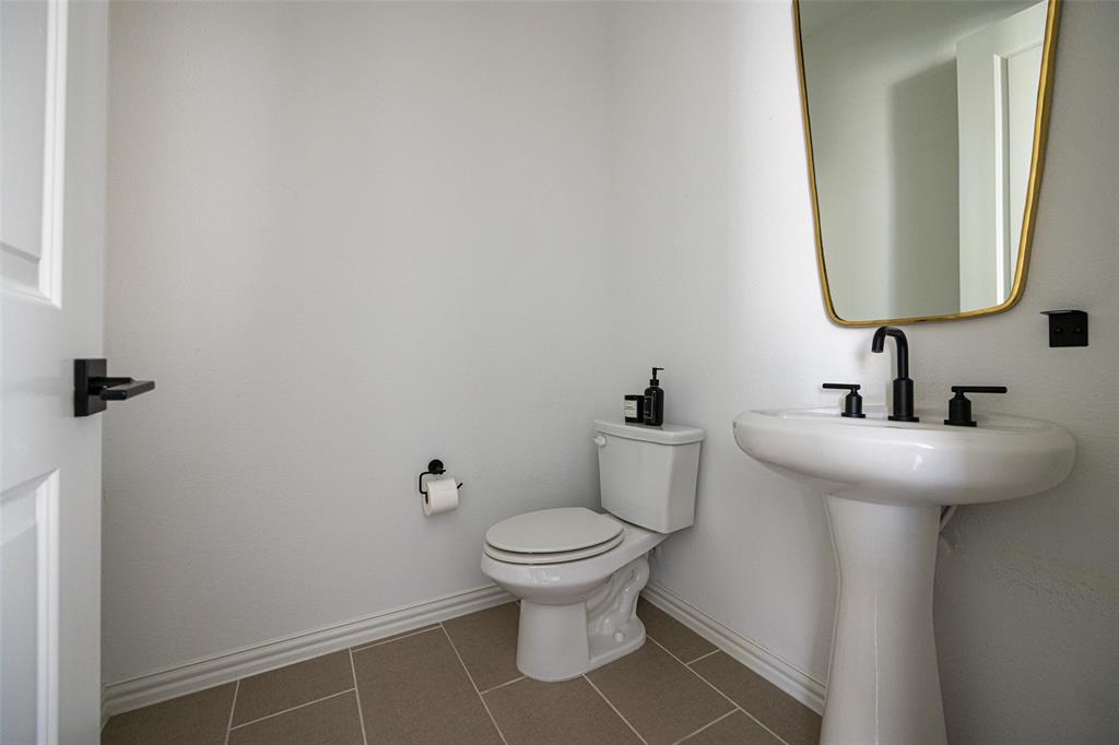 7537 Laburnam Road Dallas, TX 75228 - Photo 12 of 30 Bright powder room featuring dual pedestal sinks with chrome faucets, a ceramic toilet with elongated bowl, and neutral tile flooring