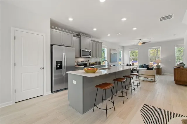 a kitchen with stainless steel appliances kitchen island granite countertop a refrigerator a sink a stove and white cabinets with wooden floor