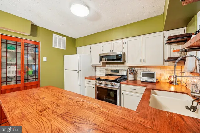 a kitchen with stainless steel appliances granite countertop a refrigerator a stove top oven a sink dishwasher and white cabinets with wooden floor