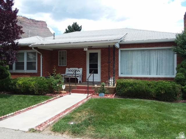 Single story home featuring a front yard, covered porch, brick siding, and a shingled roof
