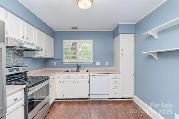 a white kitchen with a sink and dishwasher a stove top oven with wooden floor