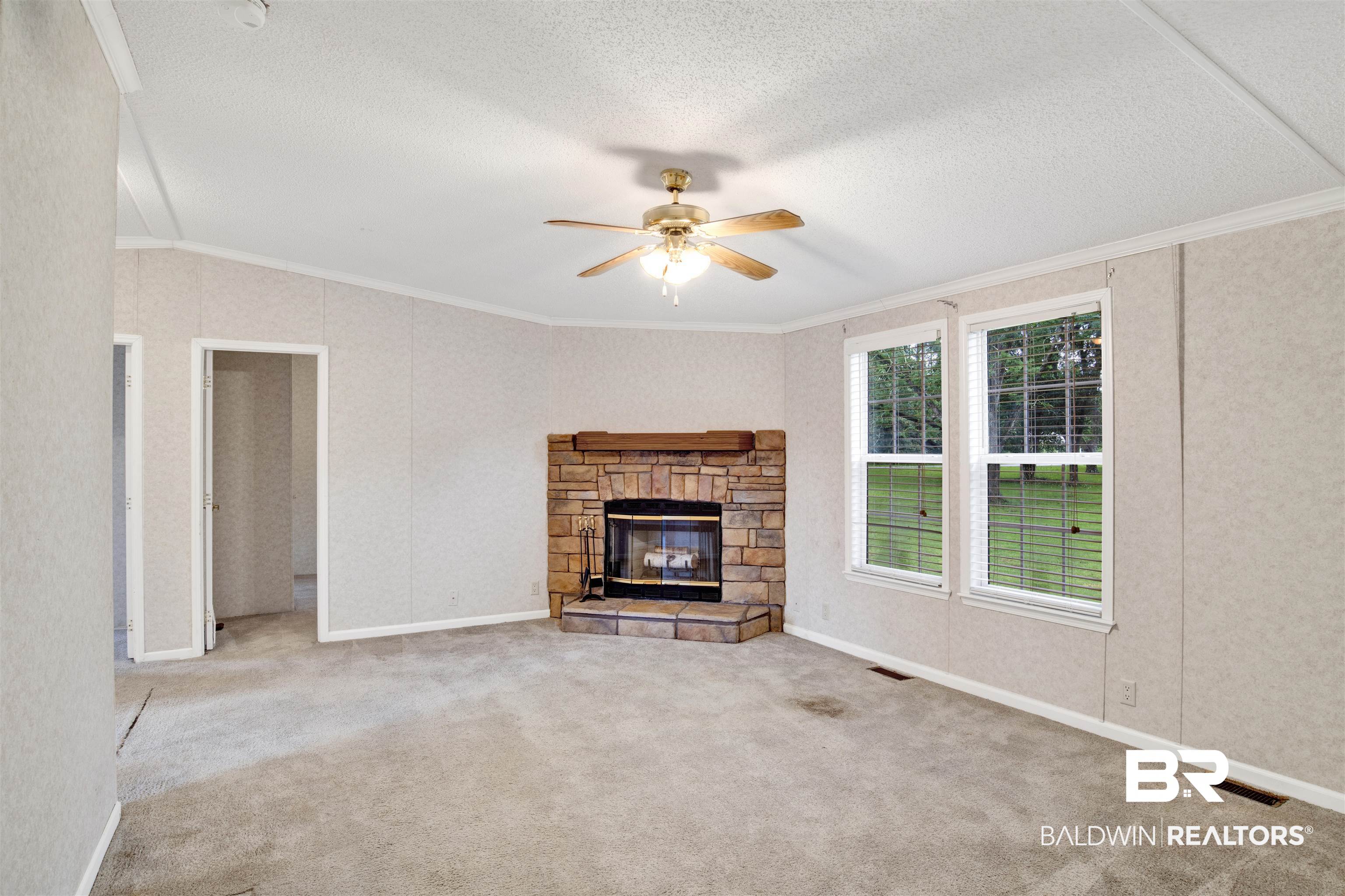 25700 County Road 71 Robertsdale, AL 36567 - Photo 13 of 40 Unfurnished living room featuring crown molding, ceiling fan, a textured ceiling, carpet, and a stone fireplace