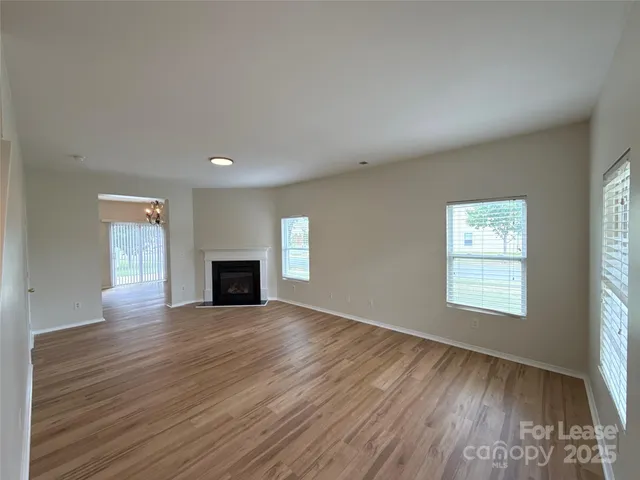 an empty room with wooden floor fireplace and windows