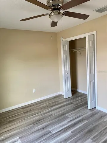 a view of an empty room with wooden floor and a ceiling fan