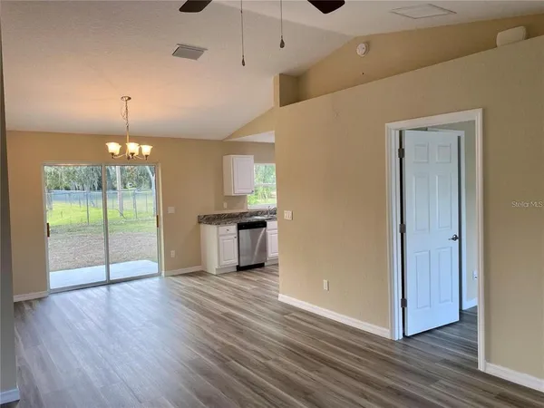 a view of an empty room with wooden floor and a kitchen
