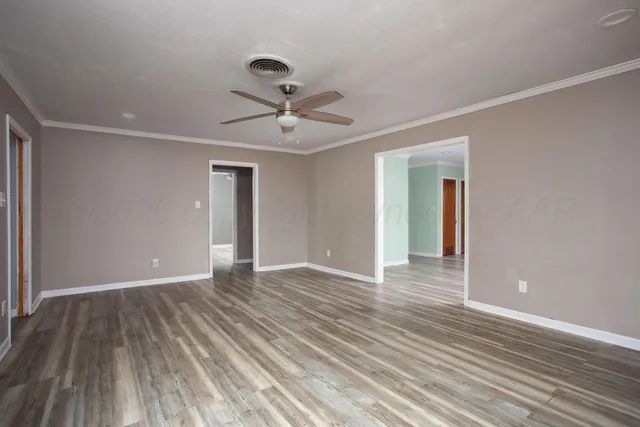 a view of an empty room with wooden floor and a ceiling fan