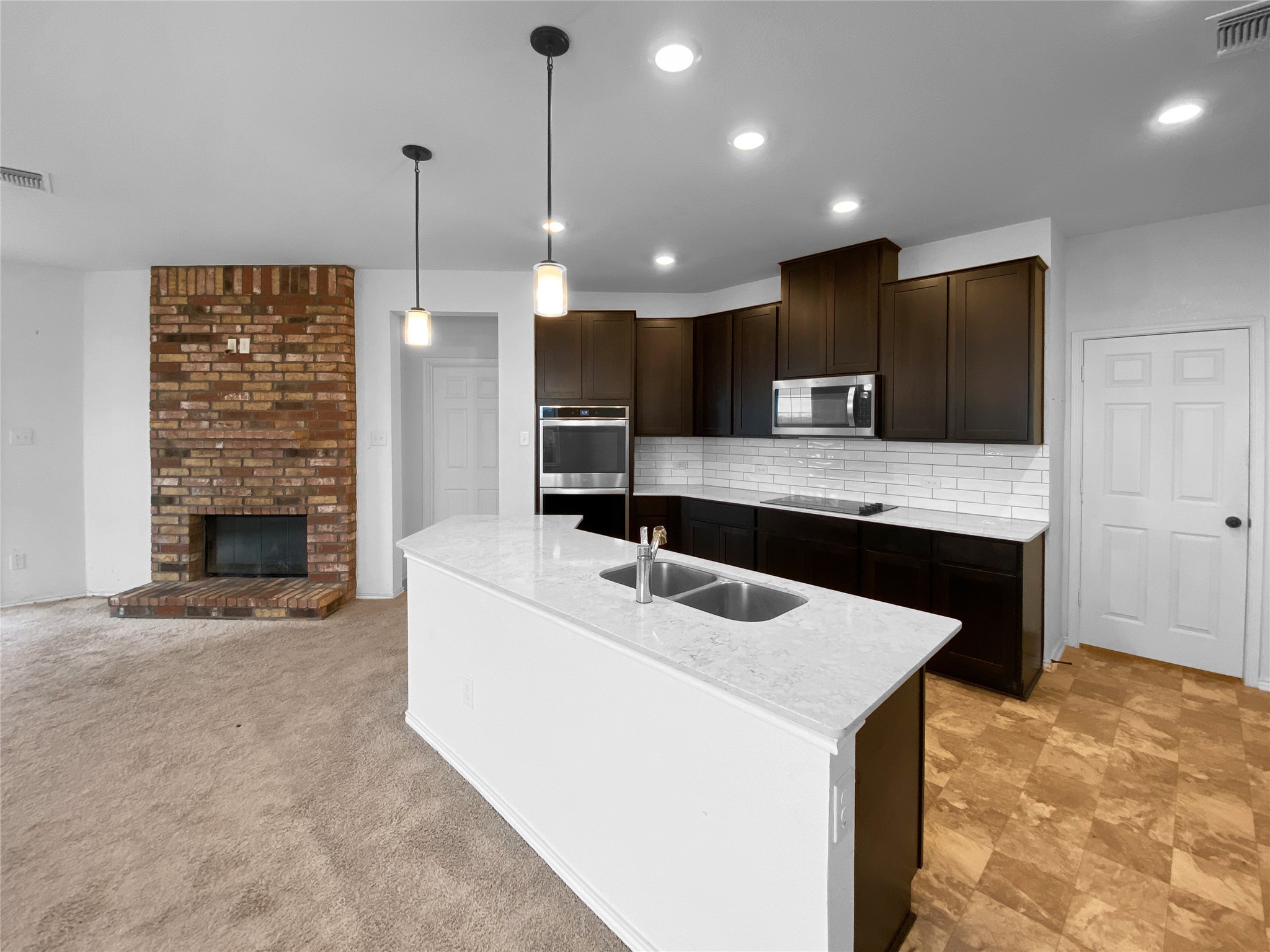 932 Yellow Ribbon Trail Jarrell, TX 76537 - Photo 8 of 26 Kitchen featuring dark wood finish cabinets, light stone counters, decorative light fixtures, an island with sink, and decorative backsplash