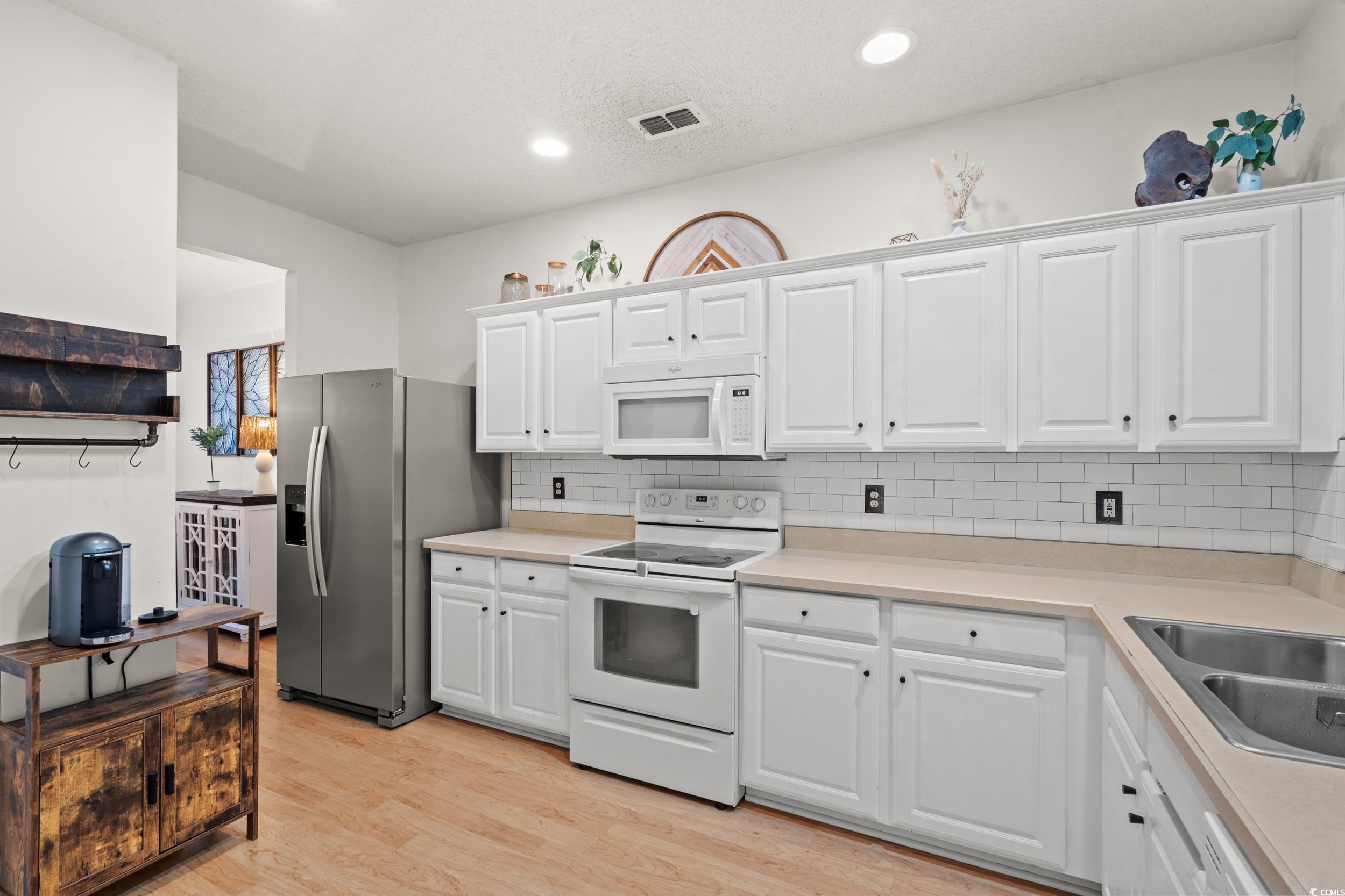104 Olde Towne Way, Unit 5 Myrtle Beach, SC 29588 - Photo 6 of 24 Kitchen with white appliances, light countertops, white cabinets, backsplash, and light wood-style floors