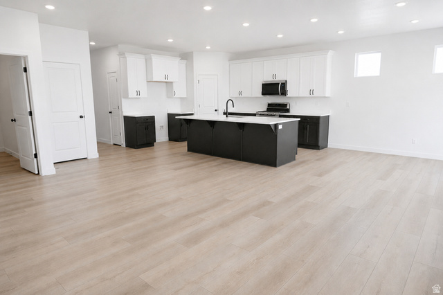1004 West Paramount Cove South, Unit 315 Ogden, UT 84405 - Photo 14 of 42 Open-concept kitchen featuring an oversized island with dark cabinetry, stainless steel appliances, light wood-finish flooring, recessed lighting, and white upper and dark lower cabinetry