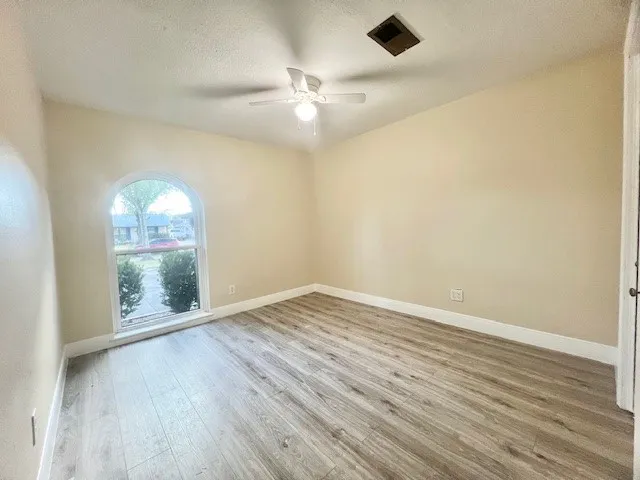 an empty room with wooden floor fan and windows