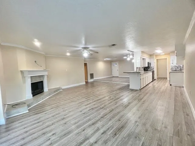 a view of an empty room and kitchen view with wooden floor