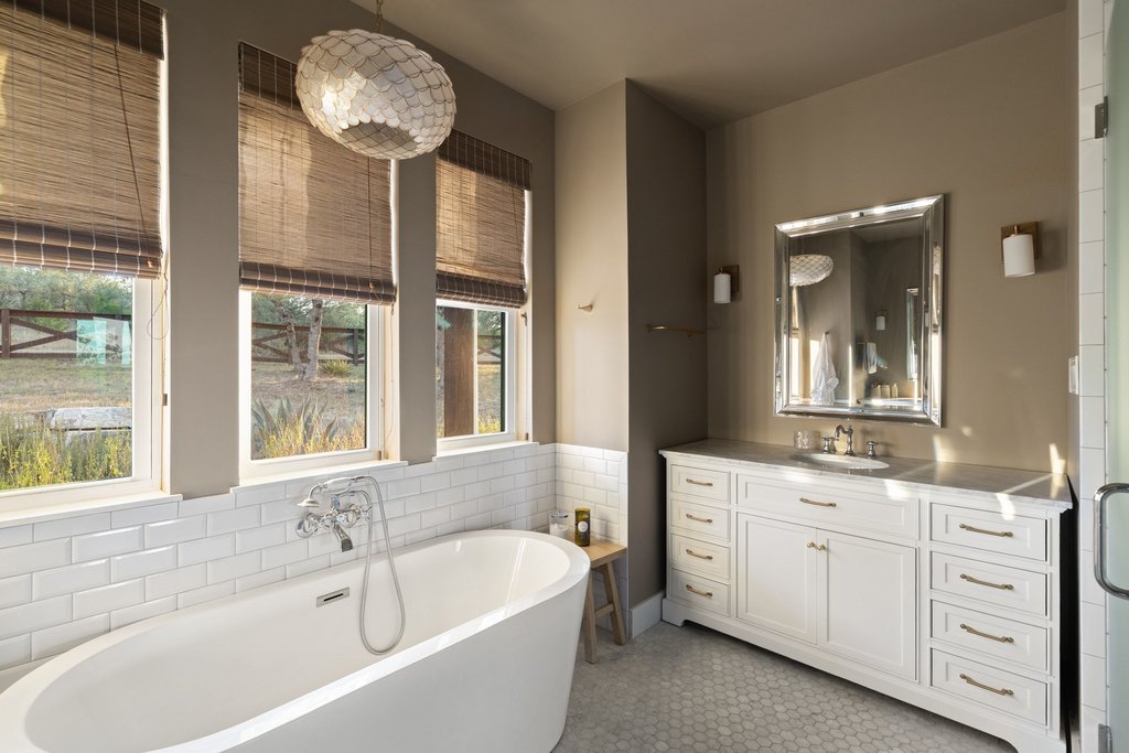 32045 Mirela Ann Road Dripping Springs, TX 78620 - Photo 15 of 30 A freestanding soaking tub rests beneath large windows alongside a classic white vanity.