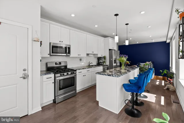 a kitchen with kitchen island granite countertop a sink a stove a refrigerator and a dining table with wooden floor