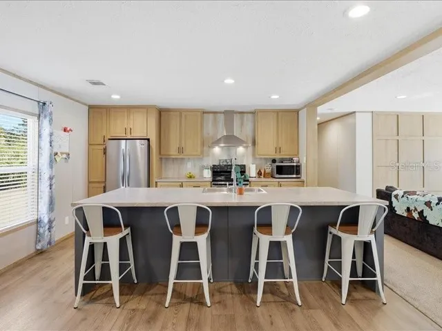 a kitchen with stainless steel appliances granite countertop a stove a refrigerator a sink a dining table and chairs with wooden floor