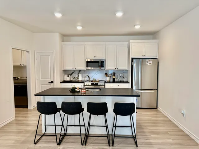 a kitchen with stainless steel appliances kitchen island granite countertop a refrigerator a stove a sink and chairs with wooden floor