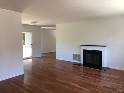 a view of an empty room with wooden floor and a fireplace