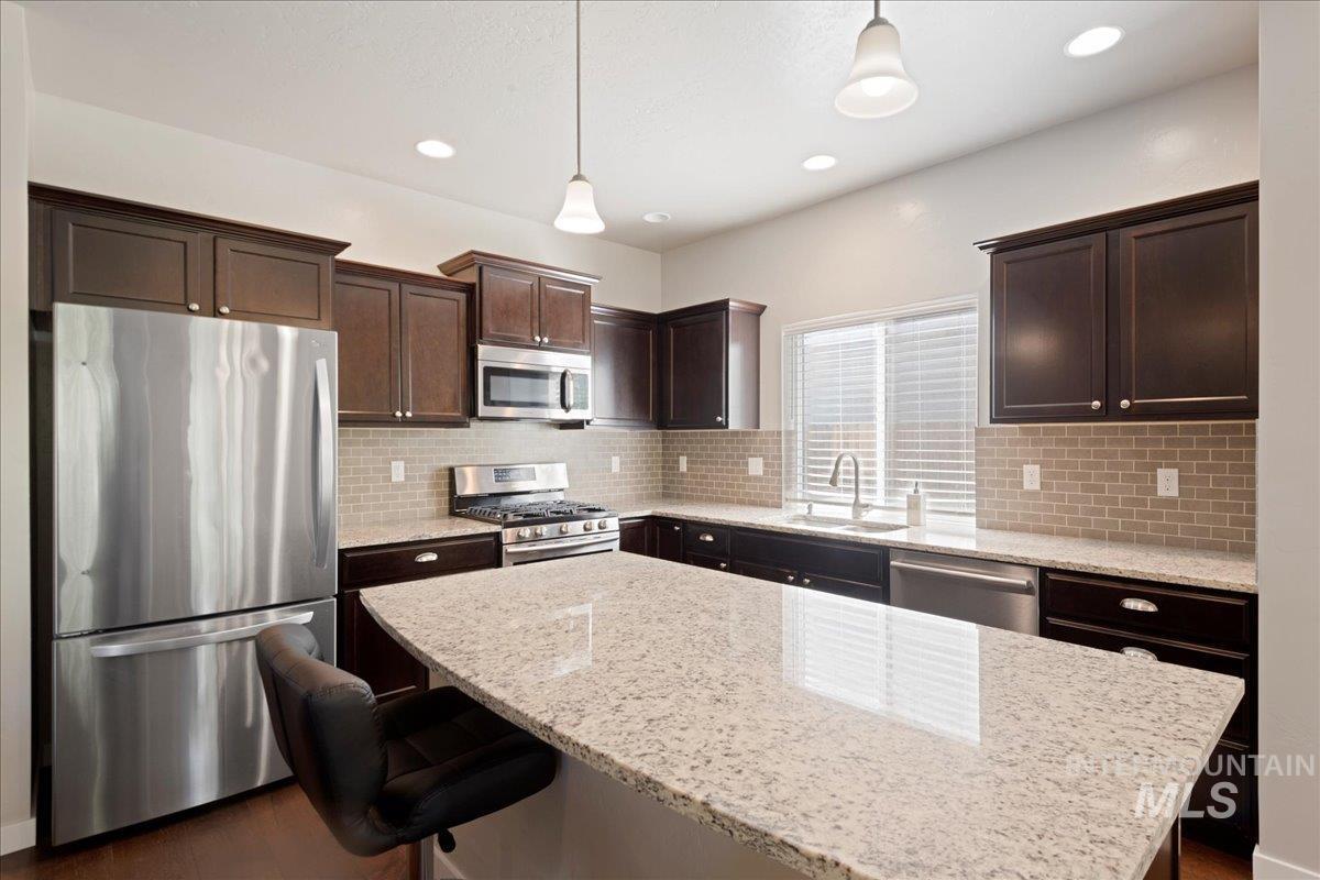 401 East Joshua Tree Drive Meridian, ID 83646 - Photo 11 of 32 Kitchen featuring stainless steel appliances, dark brown cabinetry, backsplash, pendant lighting, and a kitchen bar