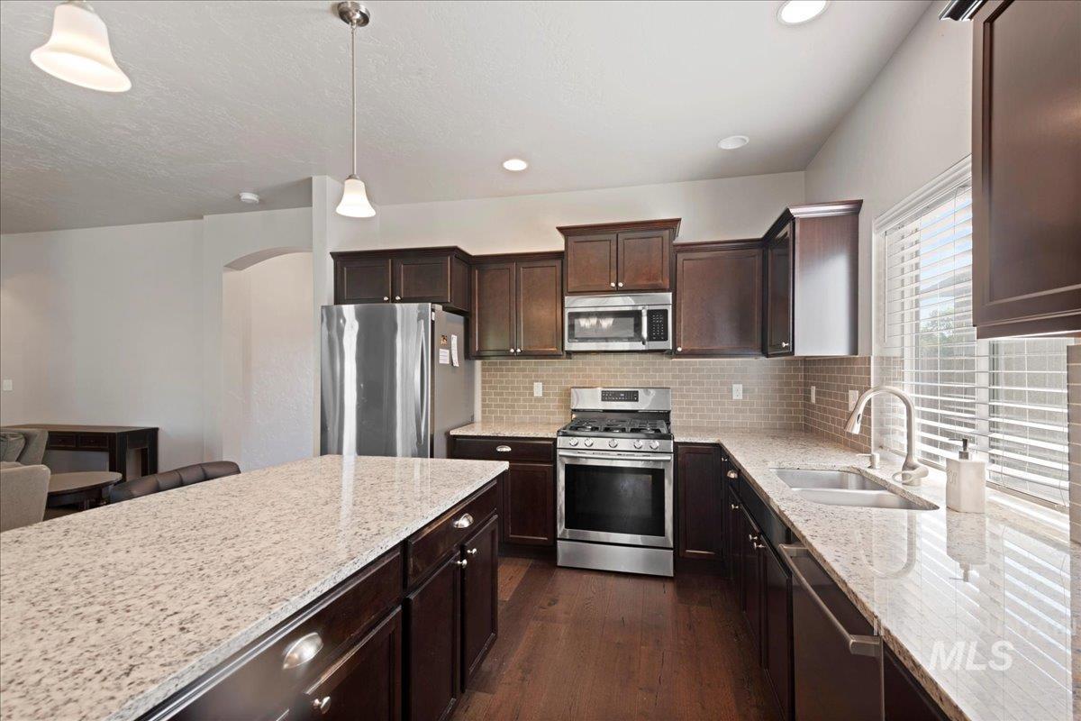 401 East Joshua Tree Drive Meridian, ID 83646 - Photo 12 of 32 Kitchen with stainless steel appliances, dark wood-type flooring, light stone countertops, dark brown cabinets, and recessed lighting