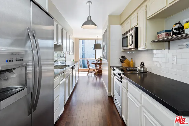 a kitchen with stainless steel appliances granite countertop a refrigerator a sink dishwasher a stove and a dining table next to a window