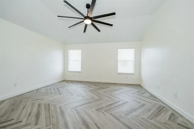 an empty room with wooden floor ceiling fan and windows