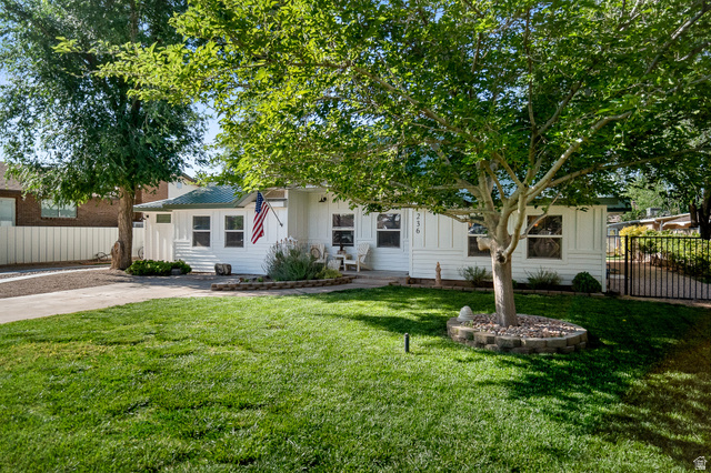 236 West 300 South Hurricane, UT 84737 - Photo 3 of 76 White-sided exterior featuring a green metal roof, front yard lawn, mature trees, and a decorative stone-lined planting bed
