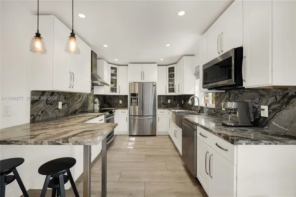 a kitchen with stainless steel appliances granite countertop a stove top oven a sink a refrigerator a dining table and chairs