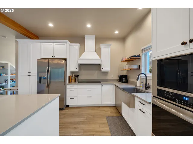a kitchen with stainless steel appliances kitchen island granite countertop a refrigerator oven a sink dishwasher and white cabinets with wooden floor