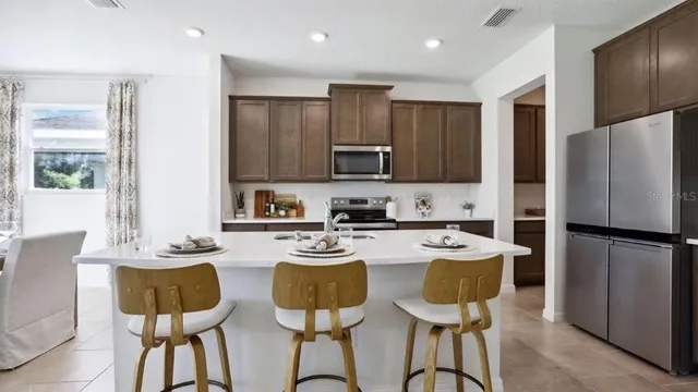 a kitchen with stainless steel appliances granite countertop a dining table chairs refrigerator and microwave