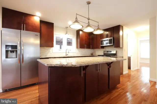 a kitchen with stainless steel appliances granite countertop a sink a refrigerator and a wooden floor