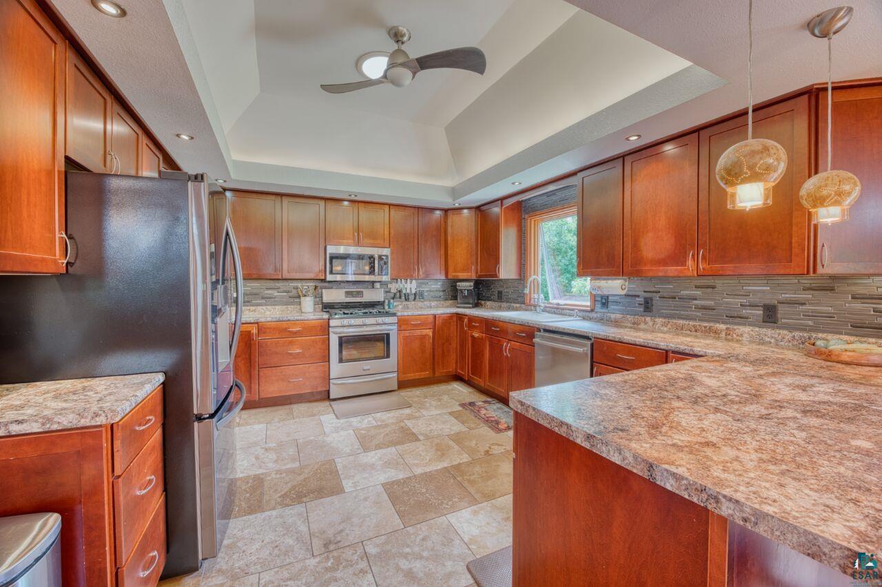 3935 Saari Road Hibbing, MN 55746 - Photo 8 of 48 Kitchen with stainless steel appliances, backsplash, hanging light fixtures, ceiling fan, and a raised ceiling