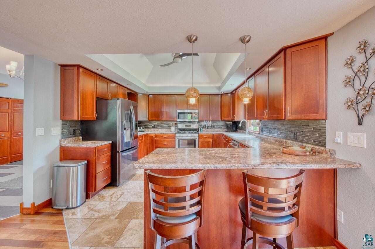 3935 Saari Road Hibbing, MN 55746 - Photo 10 of 48 Kitchen featuring stainless steel appliances, light hardwood / wood-style flooring, a tray ceiling, kitchen peninsula, and backsplash