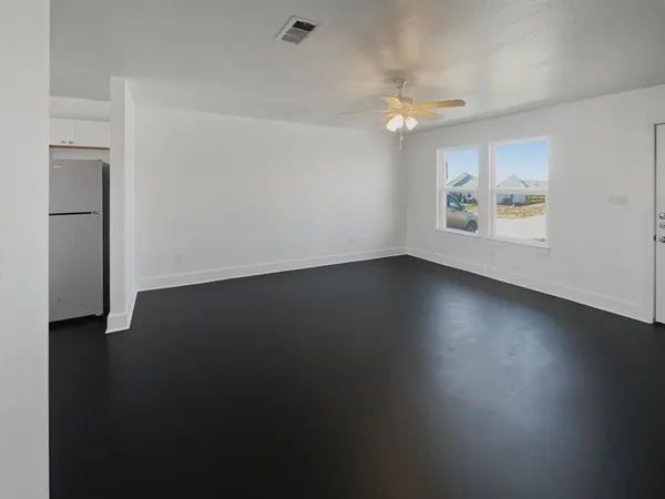 an empty room with wooden floor chandelier fan and windows